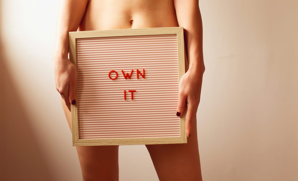 A woman holding a sign over her pelvis that says "own it"