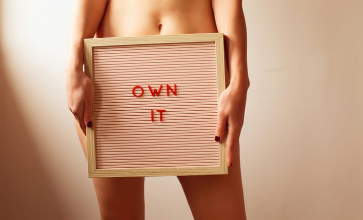 A woman holding a sign over her pelvis that says "own it"